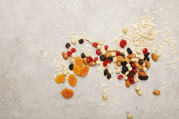 Vista superior de copos de avena, albaricoques secos y bayas, frutos secos desordenados dispersos en la mesa de superficie gris texturizada - foto de stock