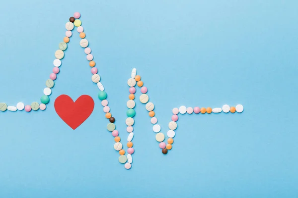 Flat lay com pílulas coloridas e coração de papel em azul — Fotografia de Stock