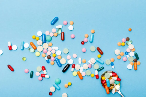 Vista superior de pílulas coloridas e colher na superfície azul — Fotografia de Stock