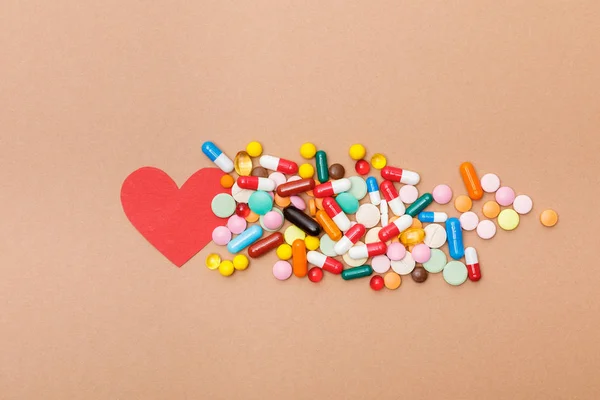 Visão superior de pílulas coloridas e coração de papel na superfície marrom — Fotografia de Stock