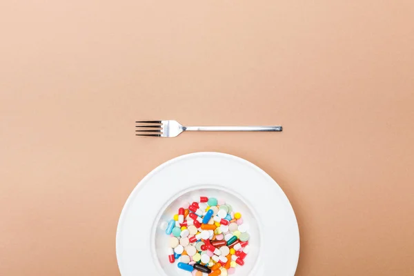 Top view of bowl with pills and fork on brown surface — Stock Photo