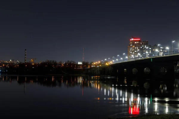 Paisaje urbano oscuro con edificios iluminados, puente y río - foto de stock