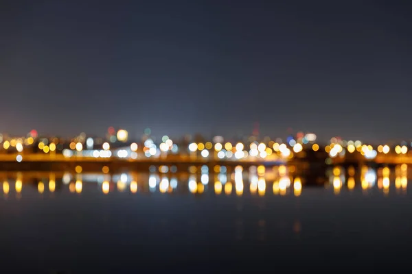 Paesaggio urbano scuro con edifici illuminati sfocati e fiume — Foto stock