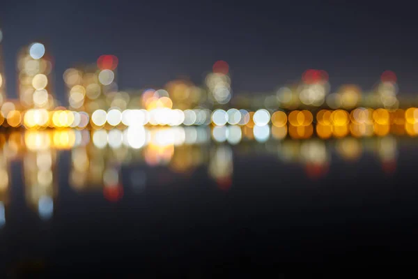 Verschwommenes dunkles Stadtbild mit beleuchteten Gebäuden, Reflexion und Bokeh-Lichtern — Stockfoto