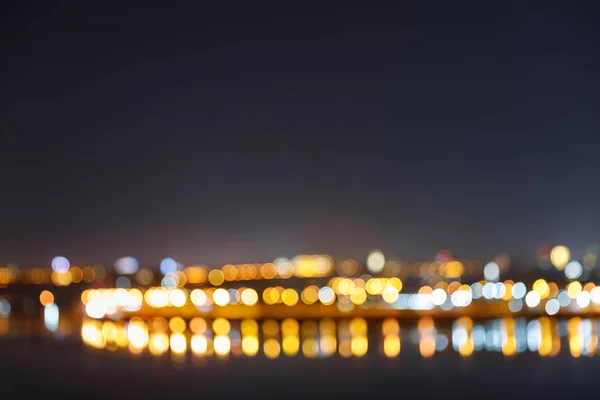 Темный городской пейзаж с освещенными размытыми зданиями, мостом и рекой — стоковое фото
