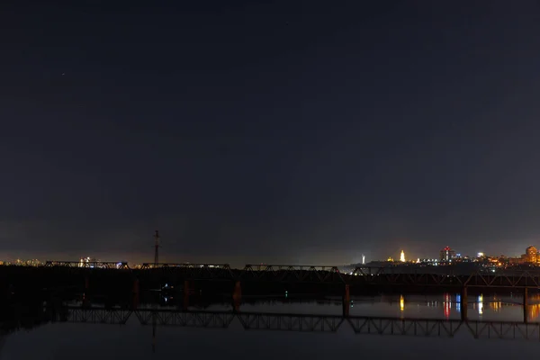 Paysage urbain sombre avec rivière tranquille et pont la nuit — Photo de stock