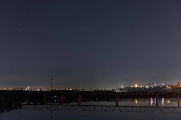 Paisaje urbano oscuro con río tranquilo y puente por la noche - foto de stock