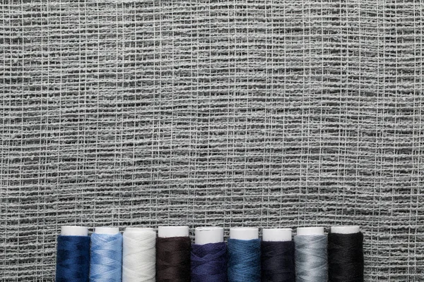 Vista superior de bobinas de hilo azul y gris en fila sobre tela de saco con espacio para copiar - foto de stock
