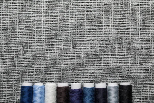 Vista superior de bobinas de hilo azul y gris en fila sobre tela de saco con espacio para copiar — Stock Photo
