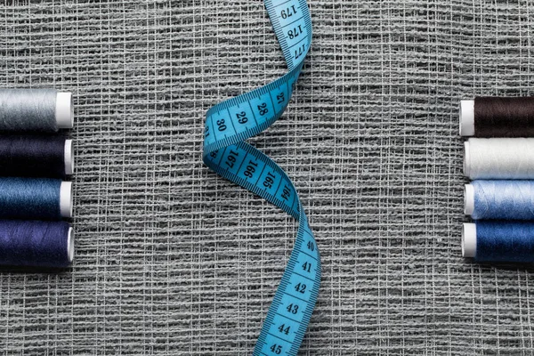 Vista superior de bobinas de hilo azul y gris con cinta métrica sobre tela de saco - foto de stock