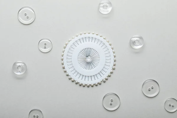 Top view of transparent clothing buttons and round container with sewing pins isolated on grey — Stock Photo