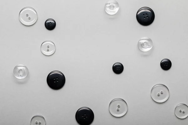 Вид сверху на прозрачные и черные кнопки одежды, изолированные на сером — стоковое фото