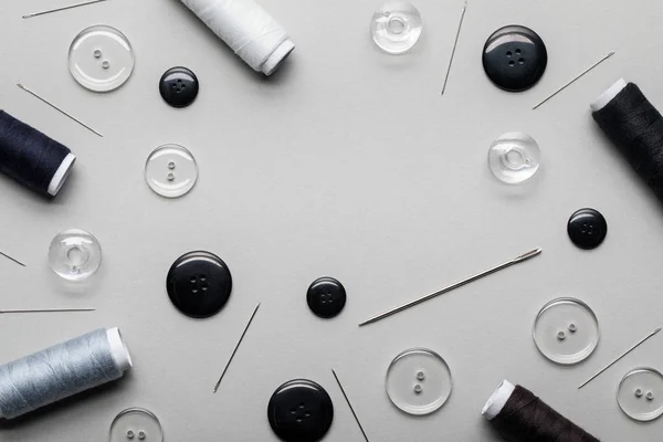 Ansicht von schwarzen und transparenten Kleidungsknöpfen, Nadeln und Fadenspulen isoliert auf grau — Stockfoto
