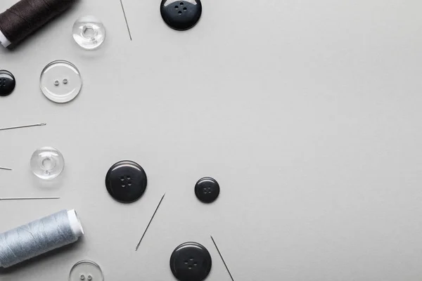 Top view of clothing buttons, needles and thread coils isolated on grey with copy space — Stock Photo