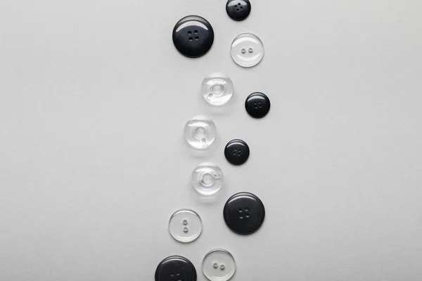 Vue de dessus des boutons de vêtements arrangés noirs et transparents isolés sur gris avec espace de copie — Photo de stock