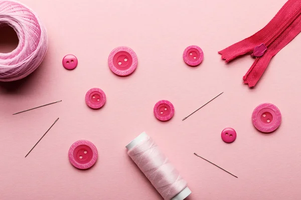 Vista superior de botones de ropa, bobina de hilo y suministros de costura aislados en rosa - foto de stock