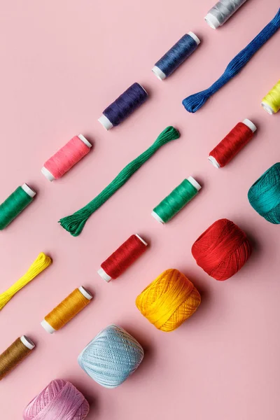 Vista superior de bolas de hilo de punto de colores, hilos de bordado y bobinas de hilo en rosa - foto de stock
