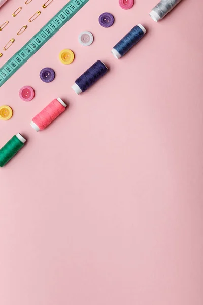 Vista superior de bobinas de hilo de colores, botones y suministros de costura aislados en rosa con espacio de copia - foto de stock