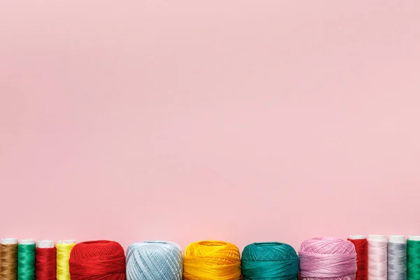 Vista dall'alto di disposti palline di filato di cotone colorato a maglia e bobine di filo isolato su rosa con spazio copia — Foto stock