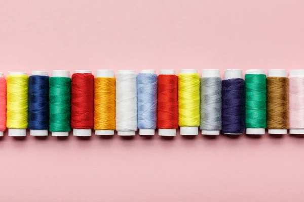 Top view of colorful thread coils in row on pink — Stock Photo