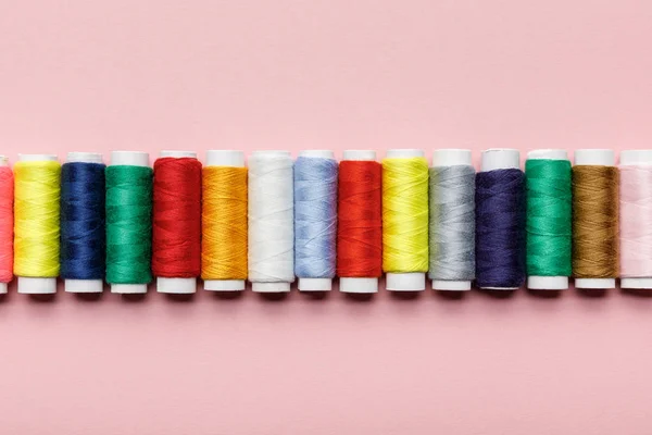 Vue de dessus des bobines de fil colorées en rangée sur rose — Photo de stock