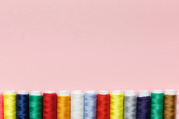 Top view of colorful thread coils in row isolated on pink with copy space — Stock Photo