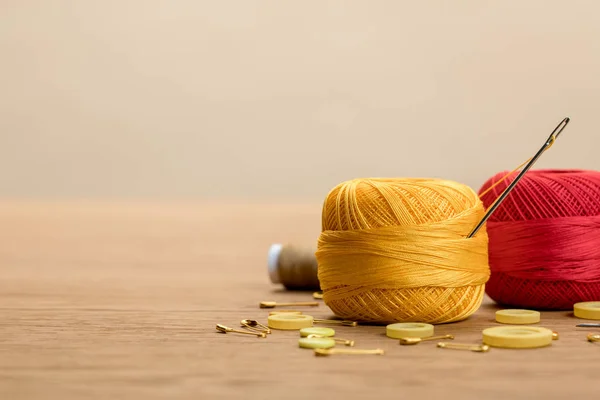 Boules de fils à tricoter en coton avec boutons de vêtements et épingles de sécurité sur table en bois isolées sur beige avec espace de copie — Photo de stock