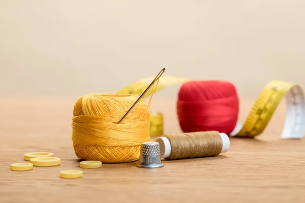 Cotton knitting yarn balls with needle and thimble on wooden table isolated on beige — Stock Photo