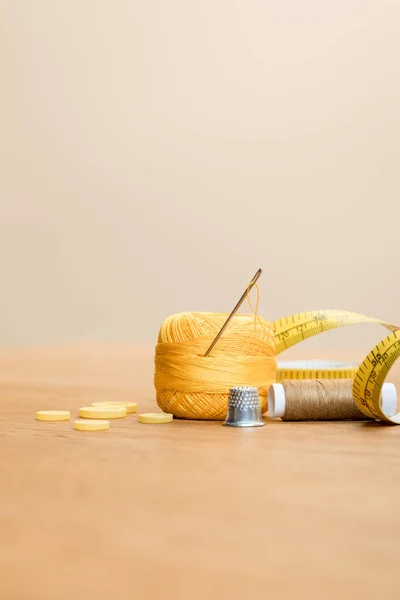 Cotton knitting yarn ball with thimble and clothing buttons on wooden table isolated on beige — Stock Photo