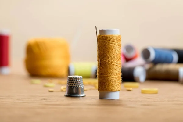 Selective focus of thread coil with thimble on wooden table isolated on beige — Stock Photo