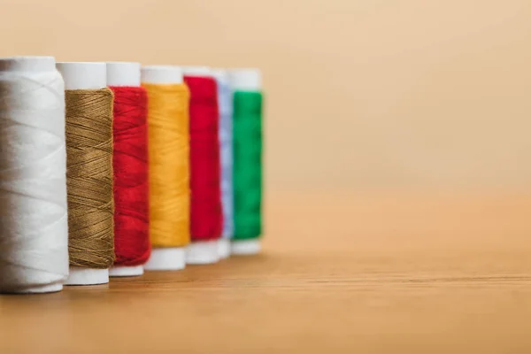Bobinas de hilo de algodón colorido en fila aislado en beige con espacio de copia - foto de stock