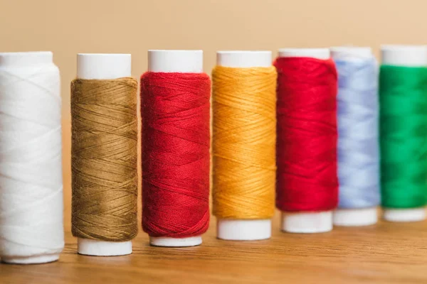 Bobinas de hilo de algodón de colores en fila en la mesa de madera aislado en beige - foto de stock