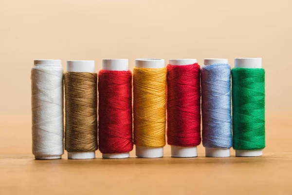 Colorful cotton thread coils in row on wooden table isolated on beige — Stock Photo
