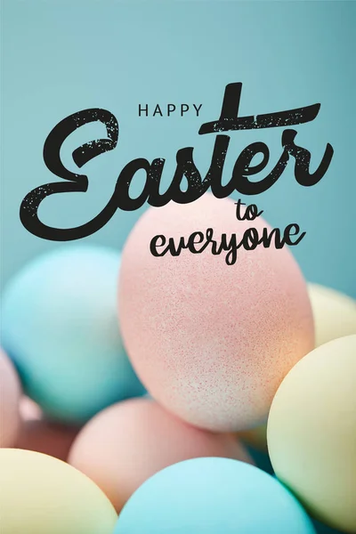Pile of multicolored painted chicken eggs with happy Easter to everyone lettering on blue background — Stock Photo