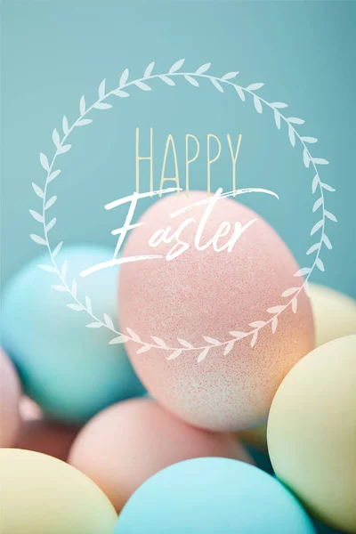 Pile of multicolored painted chicken eggs with happy Easter lettering in circle on blue background — Stock Photo