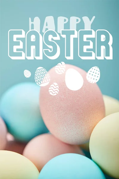 Pile of multicolored painted chicken eggs with white happy Easter lettering on blue background — Stock Photo