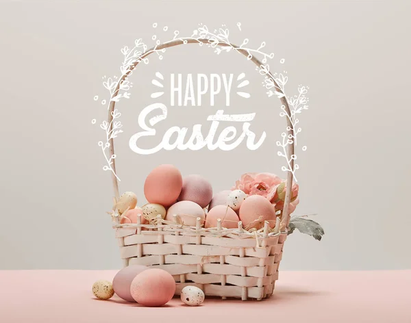 Wicker basket with pink painted eggs, flowers and happy Easter lettering on grey background — Stock Photo