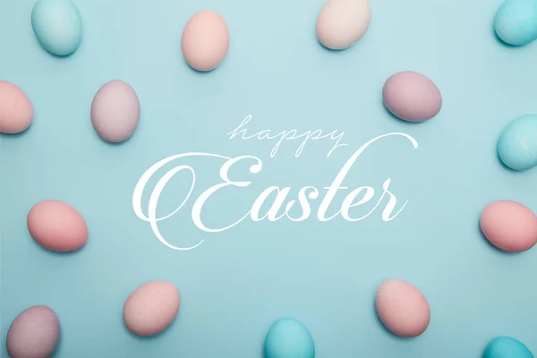 Top view of painted eggs on blue background with happy Easter lettering — Stock Photo