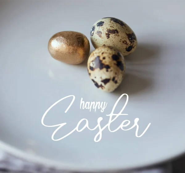 Close up of quail eggs with one painted golden on white plate with happy Easter lettering — Stock Photo