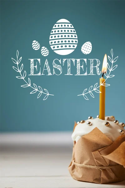 Gâteau de Pâques traditionnel avec bougie allumée sur fond bleu avec lettrage de Pâques — Photo de stock