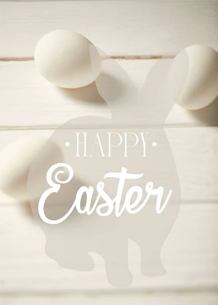Ovos de galinha na mesa de madeira branca com letras felizes da Páscoa e ilustração do coelho — Fotografia de Stock