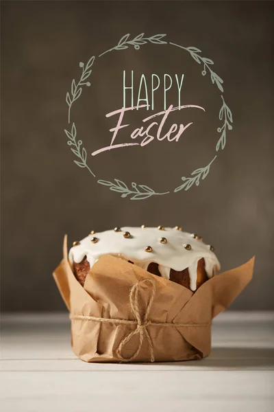 Traditional decorated Easter cake in craft paper with happy easter lettering in circle on brown background — Stock Photo