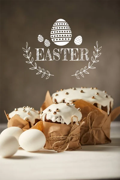 Pan tradicional de Pascua en papel artesanal y huevos blancos de pollo sobre una mesa blanca con letras de Pascua - foto de stock