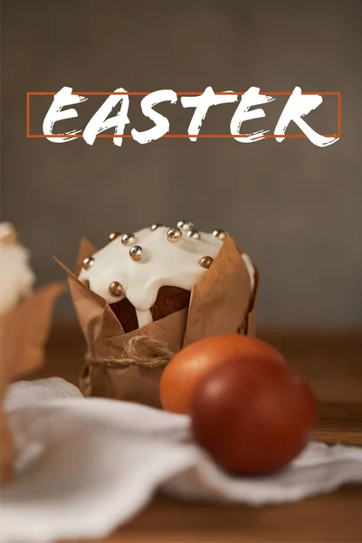 Selective focus of traditional Easter cake in craft paper and chicken eggs on napkin with easter lettering above — Stock Photo