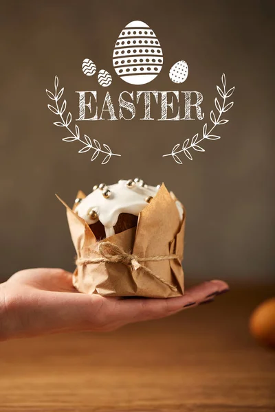 Cropped view of woman holding traditional Easter cake in craft paper with easter lettering above — Stock Photo