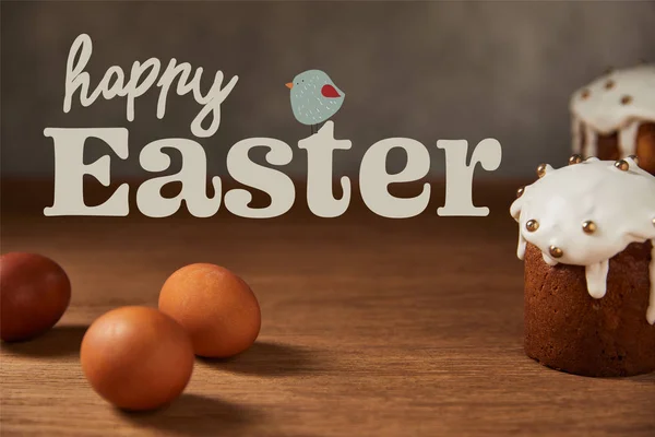 Selective focus of traditional Easter cakes and chicken eggs on wooden table with happy easter lettering and bird illustration — Stock Photo
