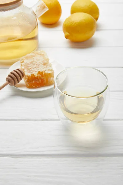 Vidro transparente e bule com chá verde, limões e favo de mel na mesa de madeira branca — Fotografia de Stock