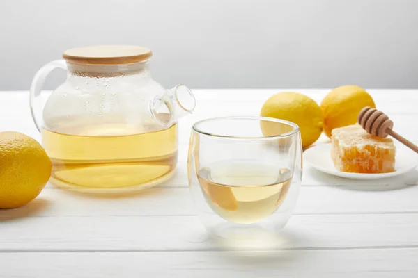 Teapot with organic herbal tea, glass, fresh lemons and honeycomb on white wooden table — Stock Photo