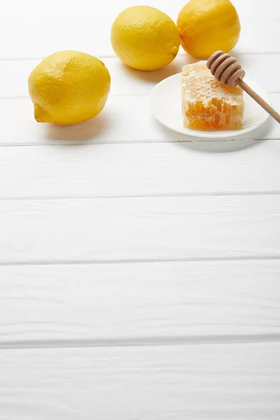 Favo de mel e gotejador de mel na placa com limões na mesa de madeira branca com espaço de cópia — Fotografia de Stock