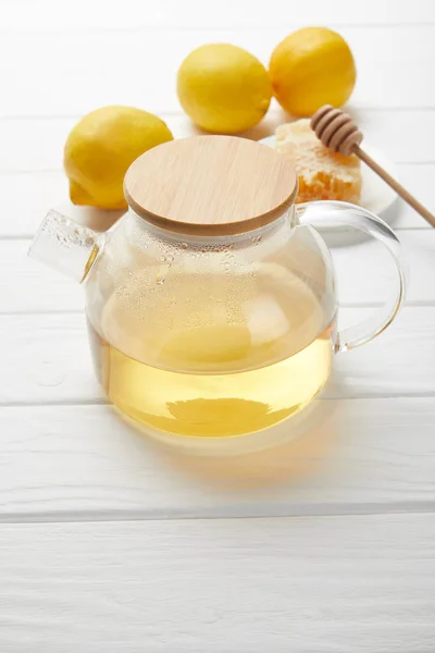 Théière transparente avec thé vert, citrons et nid d'abeille sur table en bois blanc — Photo de stock